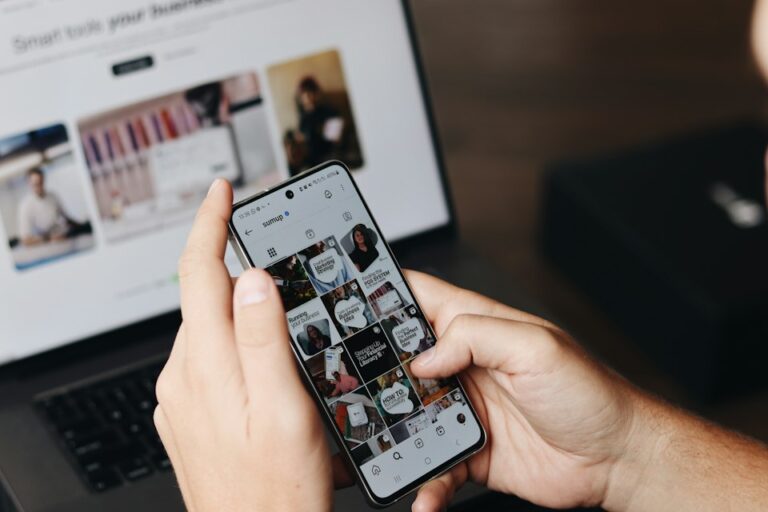 Person browsing a social media profile on a smartphone beside a laptop